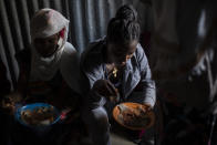 Displaced Tigrayan women, one wearing an Ethiopian Orthodox Christian cross, sit in a metal shack to eat food donated by local residents at a reception center for the internally displaced in Mekele, in the Tigray region of northern Ethiopia, on Sunday, May 9, 2021. (AP Photo/Ben Curtis)