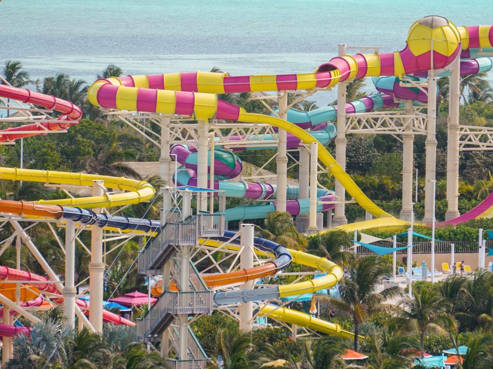 Several colorful waterslides at CocoCay with palm trees between them and ocean waters in the background