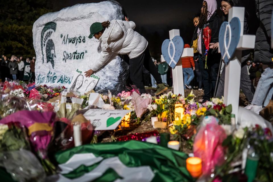 A woman leaves a sign with drawings of the three Michigan State University students killed during a vigil at The Rock on the Michigan State University campus in East Lansing on Wednesday, February 15, 2023, to honor and remember the victims of the mass shooting that happened on the MSU campus that left three dead and multiple others injured. 