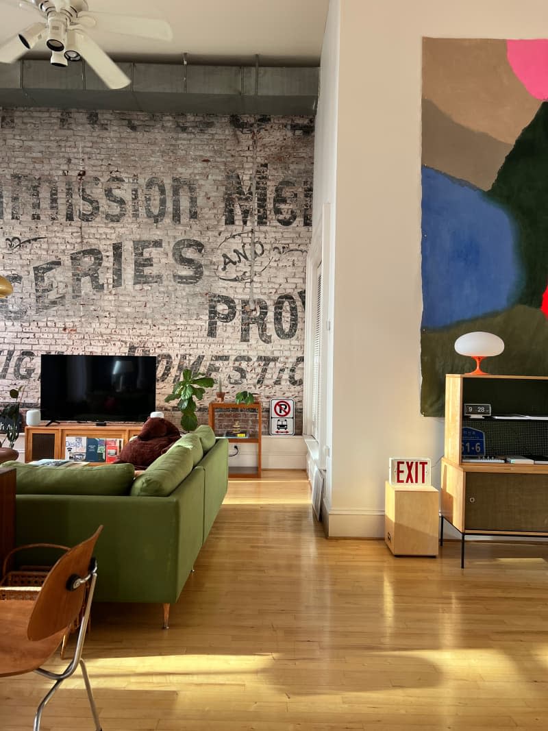 View of living room with painted brick wall in loft with light wood flooring.