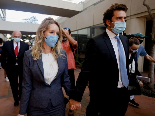 Theranos founder Elizabeth Holmes and her partner, Billy Evans, hold hands as they walk amongst a crowd outside a San Jose courthouse