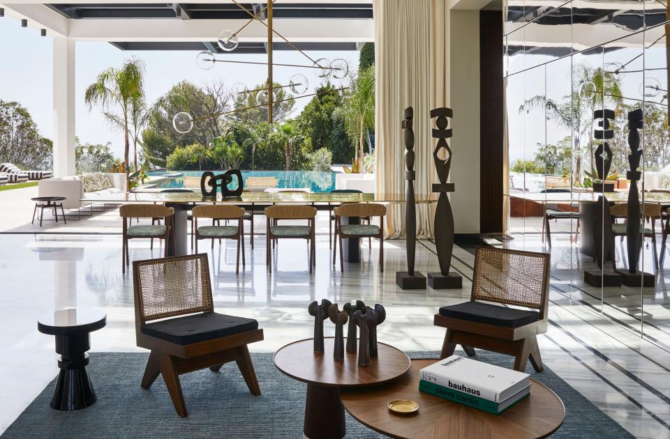 The main living area of a villa sited above Cannes and designed by Christophe Poyet and Emil Humbert of firm Humbert & Poyet opens onto the vast terrace and pool. Inside are chairs by Pierre Jeanneret from the Jacques Dworczak Collection, wooden coffee tables from Roche Bobois, a side table from Casalto and Nero Marquina marble on floors. In the background is the dining area with a Humbert & Poyet–designed table, a pendant light and chairs from Moroso, and linen curtains.