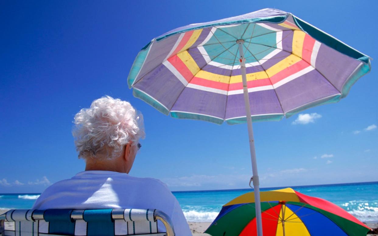 Elderly woman sits in the shade on a Florida beach - Getty
