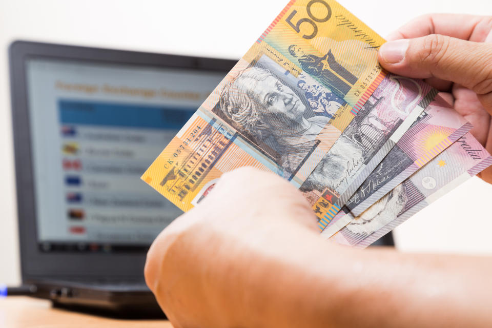 Hand holding Australian dollar in office with laptop computer as background