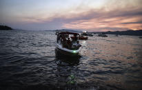 People leave with a boat as advancing fires rage Hisaronu area, Turkey, Monday, Aug. 2, 2021. For the sixth straight day, Turkish firefighters battled Monday to control the blazes that are tearing through forests near Turkey's beach destinations. Fed by strong winds and scorching temperatures, the fires that began Wednesday have left eight people dead. Residents and tourists have fled vacation resorts in flotillas of small boats or convoys of cars and trucks. (AP Photo)