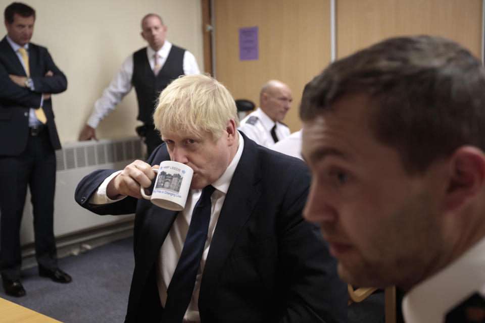 Britain's Prime Minister Boris Johnson takes a drink from a prison mug as he talks with prison staff during a visit to Leeds prison, Northern England Tuesday Aug. 13, 2019. In an announcement on Sunday Johnson promised more prisons and stronger police powers in an effort to fight violent crime. (AP Photo/Jon Super)