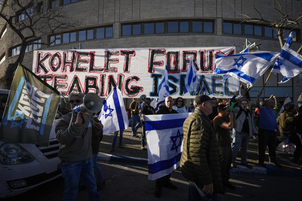 Manifestantes ondean banderas en una protesta contra el plan de reforma judicial del nuevo gobierno del primer ministro, Benjamin Netanyahu, ante las oficinas del grupo conservador Foro Kohelet, que ayudó a redactar la propuesta de ley, en Jerusalén, el jueves 9 de marzo de 2023. (AP Foto/Ohad Zwigenberg)