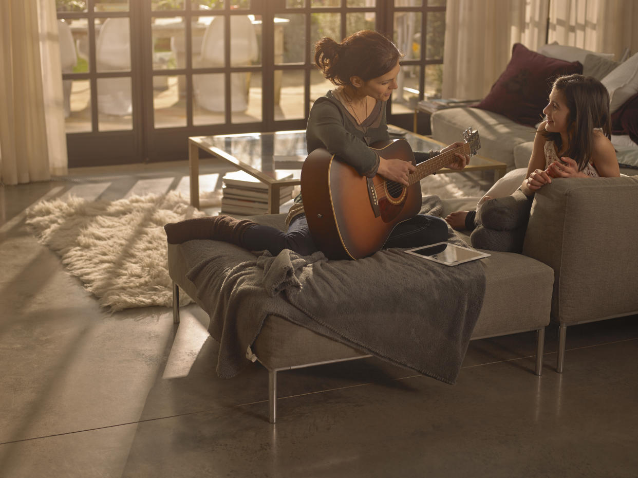 Woman on a sofa practising the guitar with her daughter.