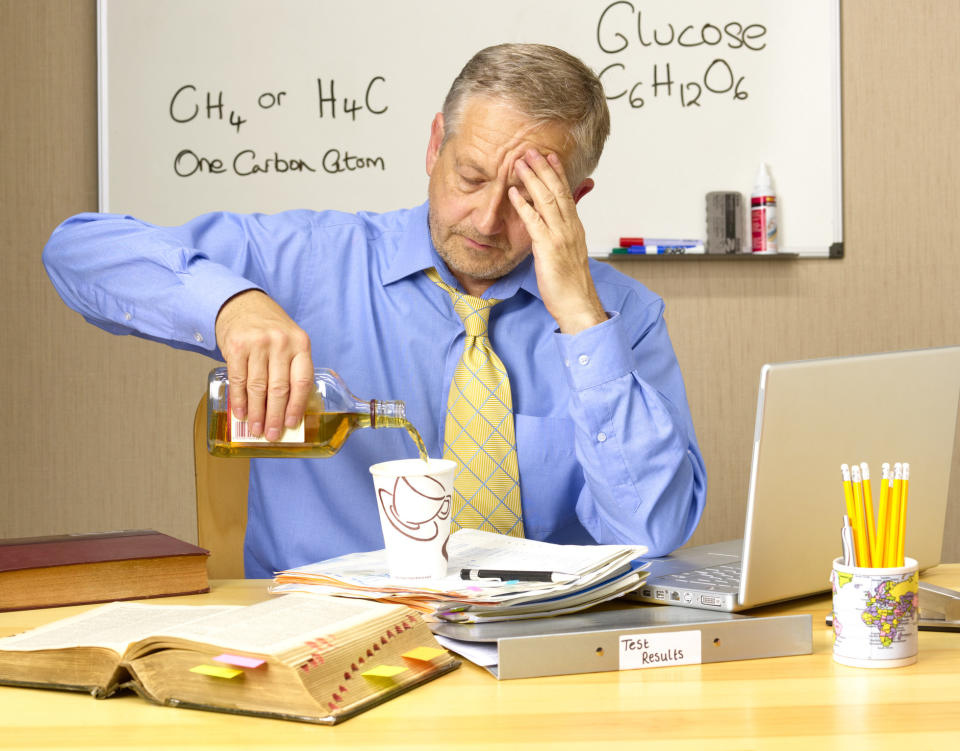 Stressed teacher pouring booze in his coffee cup