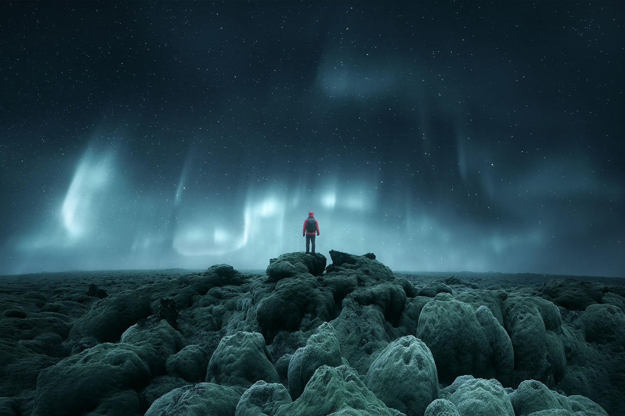 Distant silhouette of a person standing on rocks below Northern Lights Getty Images/mariuskasteckas