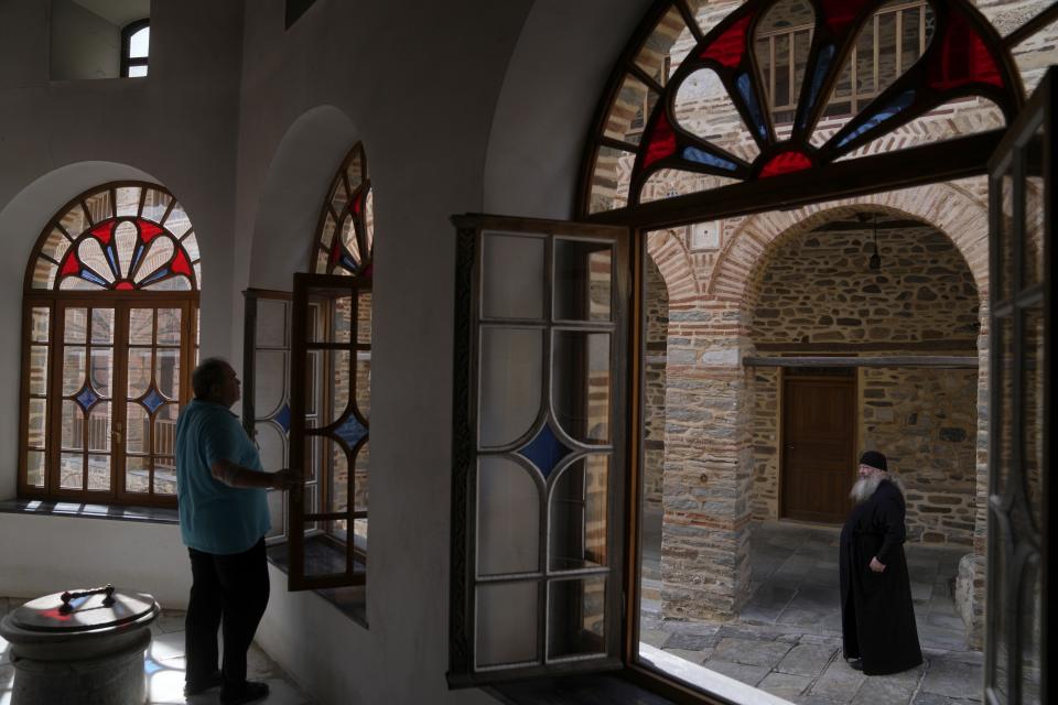 A man opens a window of the church as a monk stands at the Pantokrator Monastery in the Mount Athos, northern Greece, on Thursday, Oct. 13, 2022. Deep inside a medieval fortified monastery in the Mount Athos monastic community, researchers are for the first time tapping a virtually unknown treasure: thousands of Ottoman-era manuscripts that include the oldest of their kind in the world. (AP Photo/Thanassis Stavrakis)