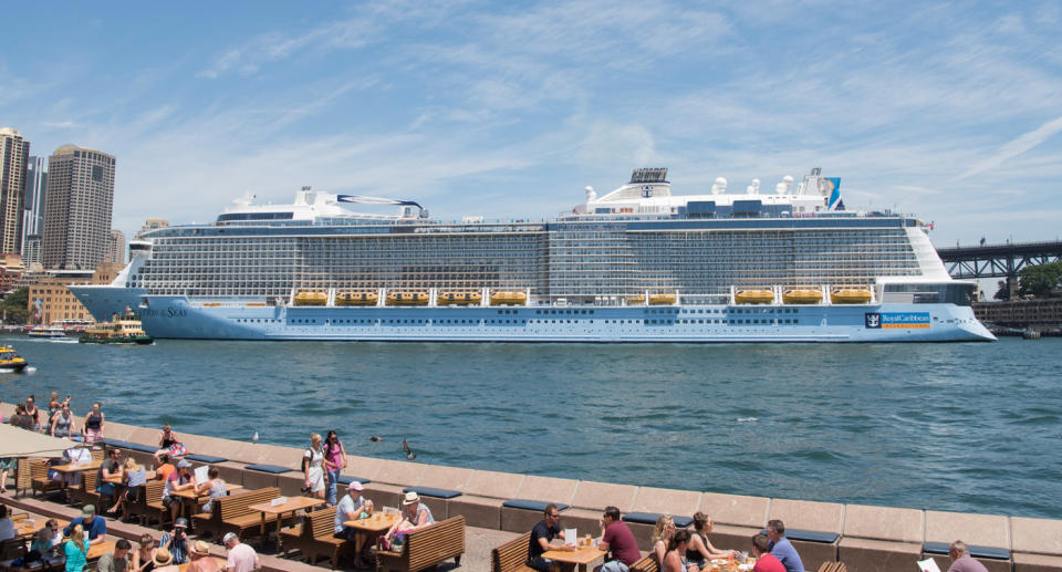 A Royal Caribbean ship docked at Sydney Harbour with diners sitting outside the Opera Bar overlooking the boat. 