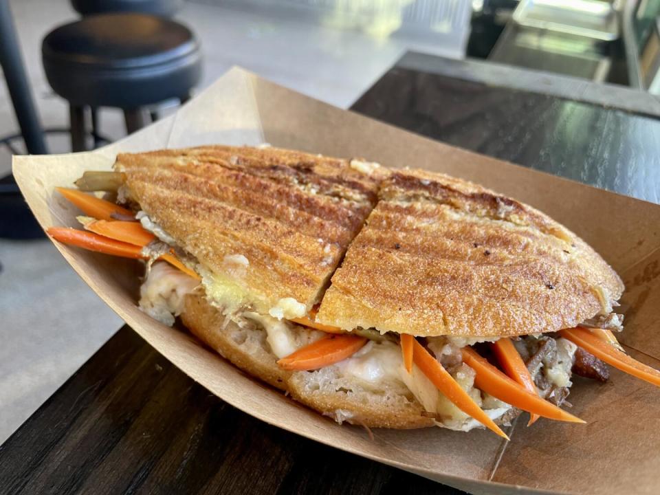 A large sandwich on a halved toasted roll, with carrots peeking out at the edges