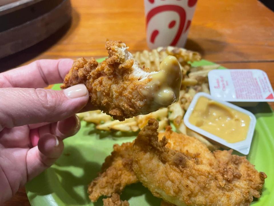 The writer holds a chicken tender with Chick-fil-A sauce on it