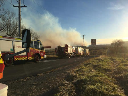 Fire engines line a road as smoke rises in the background from a bushfire in New South Wales, Australia, August 16, 2018, in this picture obtained from social media. Fire and Rescue NSW/via REUTERS