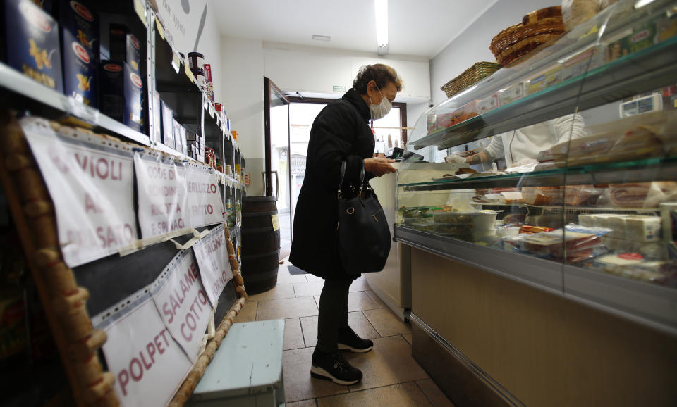 In this photo taken on Thursday, March 12, 2020, a woman buys food in a deli meat and cold cuts shop in Codogno, Italy. The northern Italian town that recorded Italy’s first coronavirus infection has offered a virtuous example to fellow Italians, now facing an unprecedented nationwide lockdown, that by staying home, trends can reverse. Infections of the new virus have not stopped in Codogno, which still has registered the most of any of the 10 Lombardy towns Italy’s original red zone, but they have slowed. For most people, the new coronavirus causes only mild or moderate symptoms. For some it can cause more severe illness. (AP Photo/Antonio Calanni)