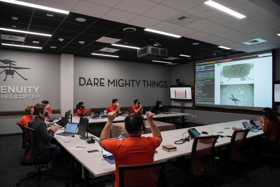 people in orange shirts wearing headsets sit around a table around a big screen showing mars helicopter data