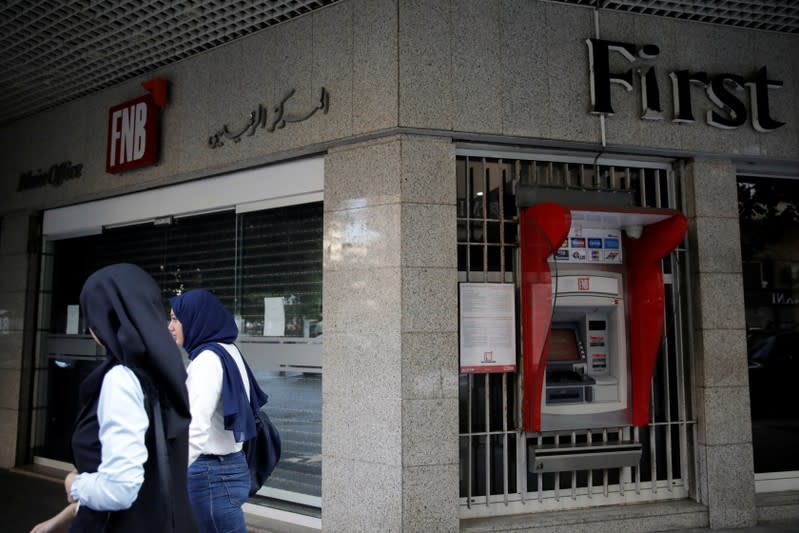 Two women walk past a closed bank office in Beirut