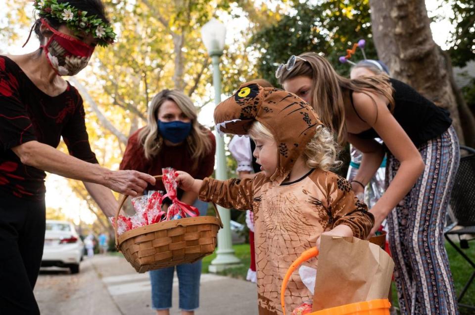 Crosby Dugger, 2, right, receives a treat bag from fellow Sonoma Way resident Debbie Loh as neighborhood children trick-or-treat on their East Sacramento block during a small “parade” on Oct. 31, 2020.