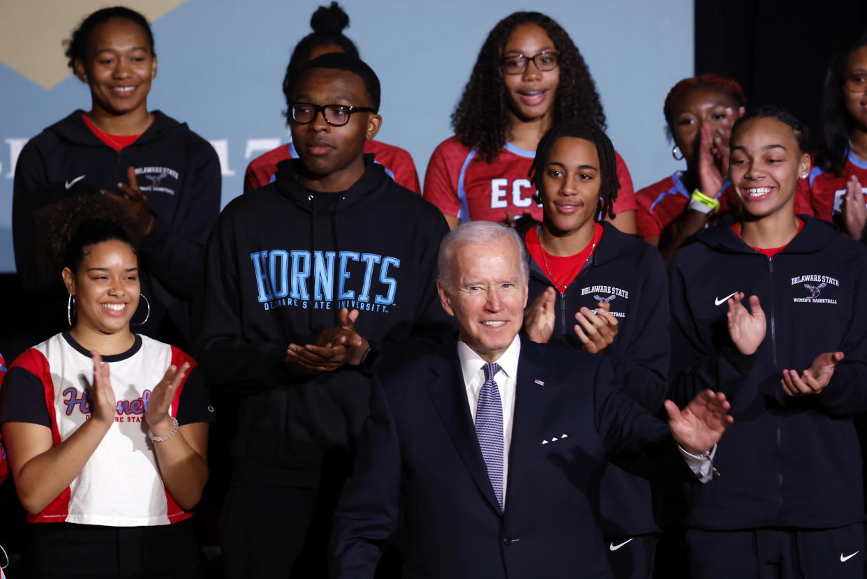 President Biden stands in front of nine students, who appear to be applauding.