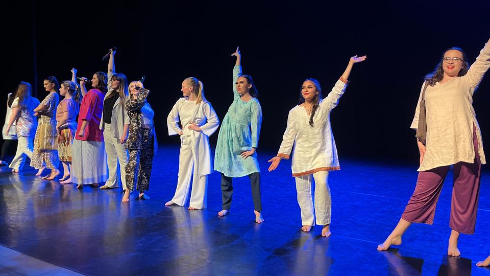 A line of women wearing colourful clothing line up on a stage