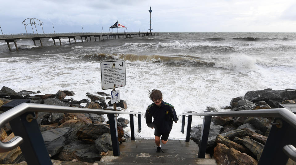A young boy runs up steps to avoid a wave as high tide and a storm surge at Brighton Jetty, Adelaide in June 2018.
