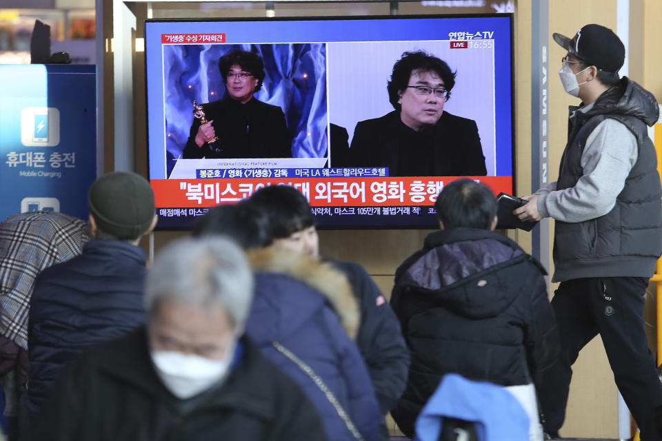 People watch a TV screen showing images of South Korean director Bong Joon Ho during a news program at the Seoul Railway Station in Seoul, South Korea, Monday, Feb. 10, 2020. In a milestone win that instantly expanded the Oscars' horizons, Bong's masterfully devious class satire "Parasite" became the first non-English language film to win best picture in the 92-year history of the Academy Awards. The signs read: "Foreign language movie." (AP Photo/Ahn Young-joon)