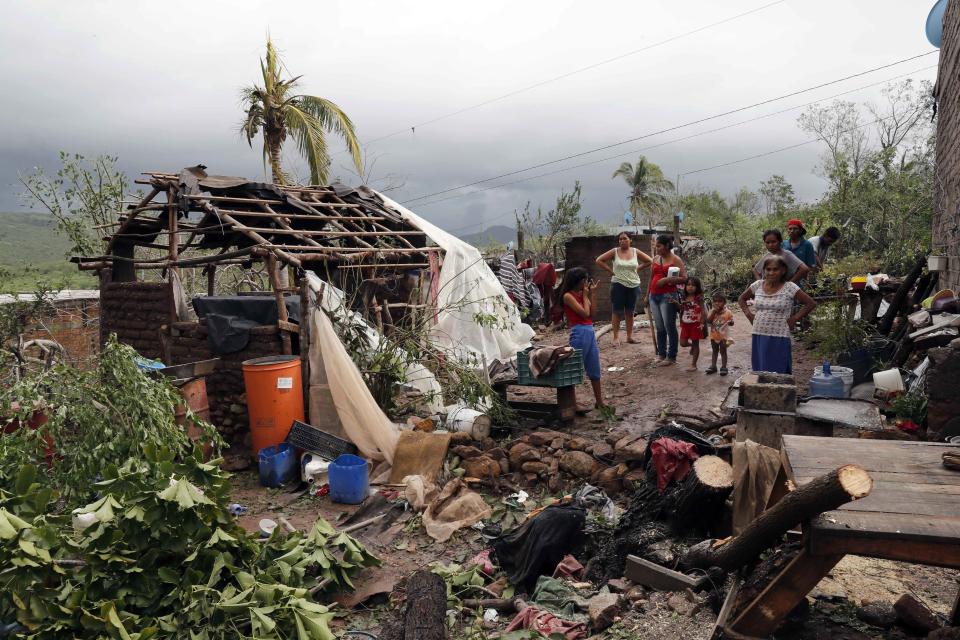 A family stands near their damaged home and debris in the aftermath of Hurricane Willa, in Escuinapa, Mexico, Wednesday, Oct. 24, 2018. Emergency workers on Wednesday were struggling to reach beach towns left incommunicado by a blow from Willa. (AP Photo/Marco Ugarte)