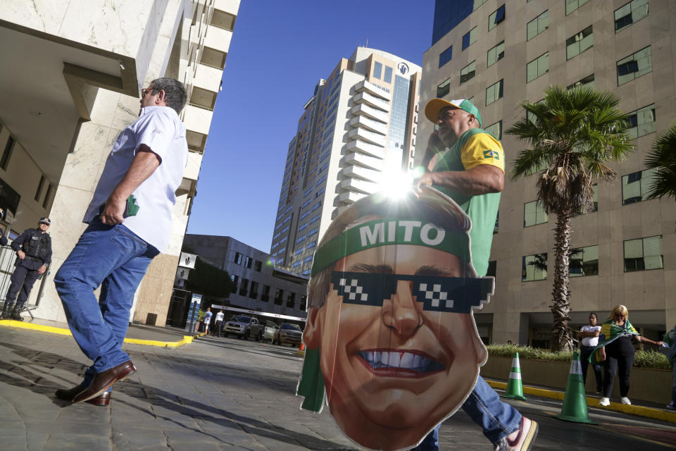 A supporter of Brazil's former President Jair Bolsonaro carries a cardboard cutout of his face outside the Liberal Party's headquarters where Bolsonaro will arrive in Brasilia, Brazil, Thursday, March 30, 2023. Bolsonaro arrived back in Brazil on Thursday after a three-month stay in Florida. (AP Photo/Gustavo Moreno)