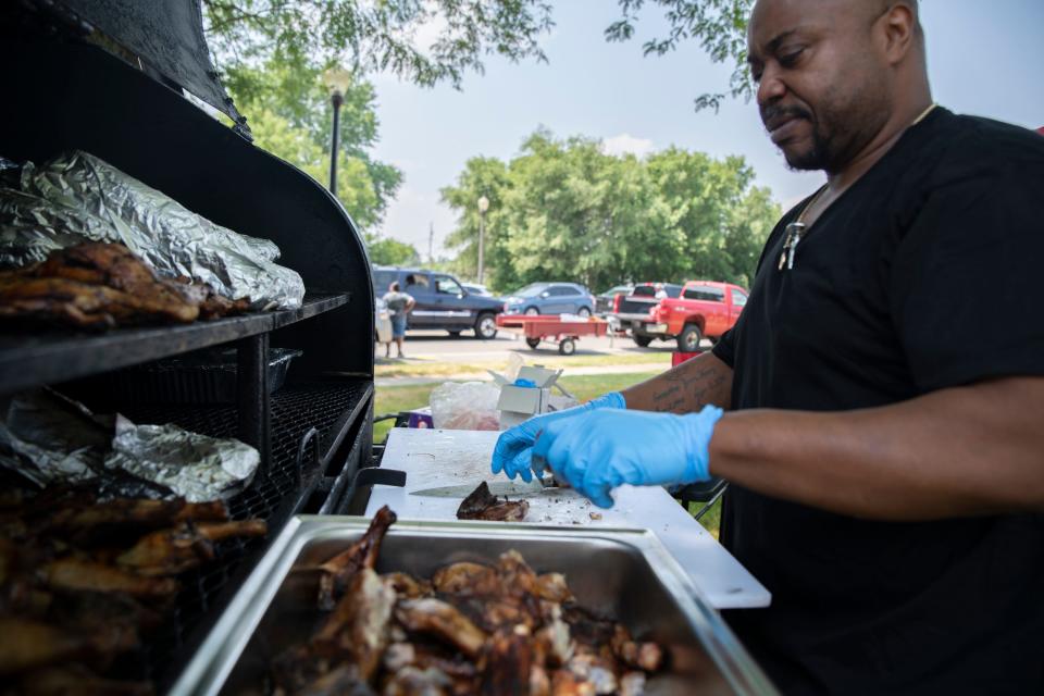 Yakini Henry of Henry’s Catering cuts barbecued chicken to sell at the Juneteenth celebration in LaSalle Park in South Bend on June 17, 2023.