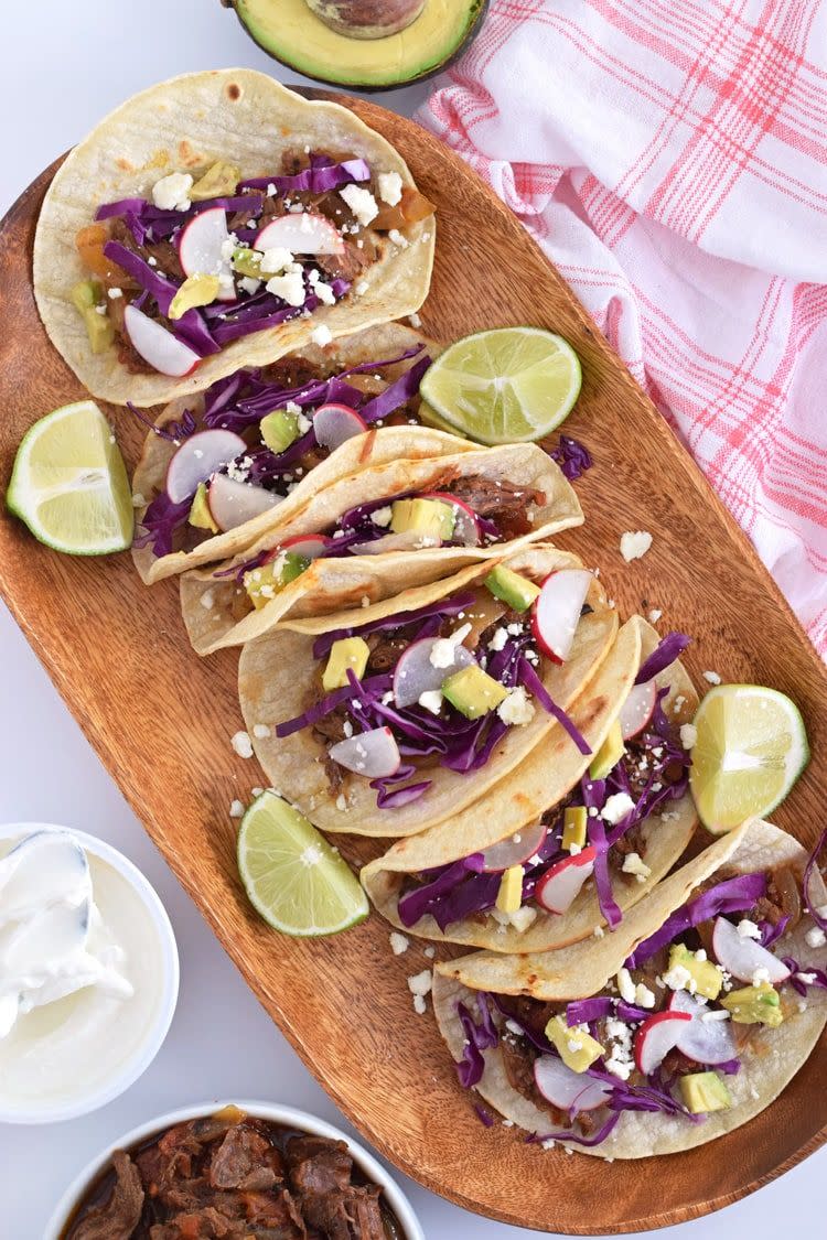 slow cooker beef tinga tacos on wood board with lime wedges