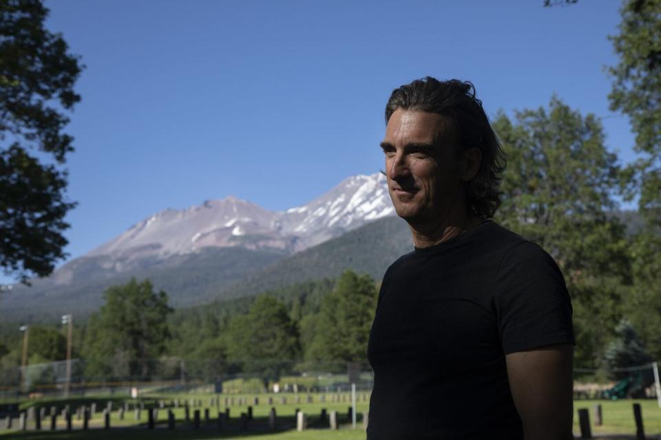 A man stands below a mountain with patches of snow