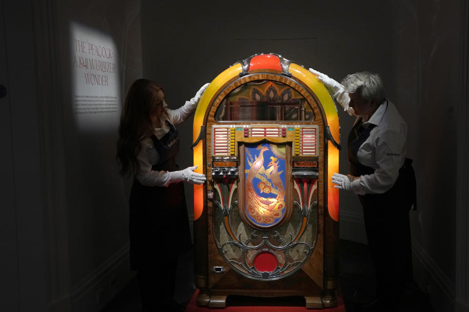 Sotheby's handlers stand with a A Wurlitzer Model 850 'Peacock' design jukebox by Paul Fuller, American, circa 1941, at Sotheby's auction rooms in London, Thursday, Aug. 3, 2023. More than 1,000 of Freddie Mercury's personal items, including his flamboyant stage costumes, handwritten drafts of “Bohemian Rhapsody” and the baby grand piano he used to compose Queen's greatest hits, are going on show in an exhibition at Sotheby's London ahead of their sale. (AP Photo/Kirsty Wigglesworth)