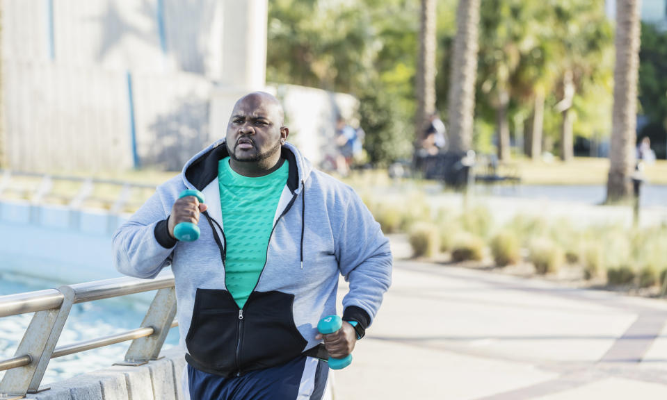 A man in a hoodie holding weights power walks.