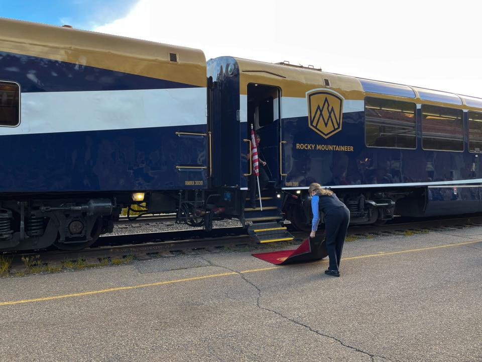 A Rocky Mountaineer train host unrolls a red carpet before passengers board the train.