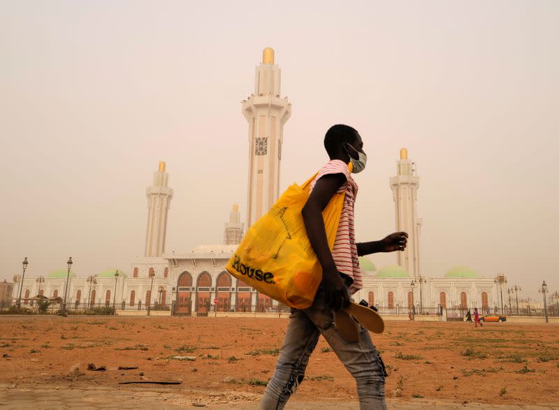 A street vendor walks past the Massalikoul Djinane mosque as dust carried by winds from the Sahara desert shrouds Dakar