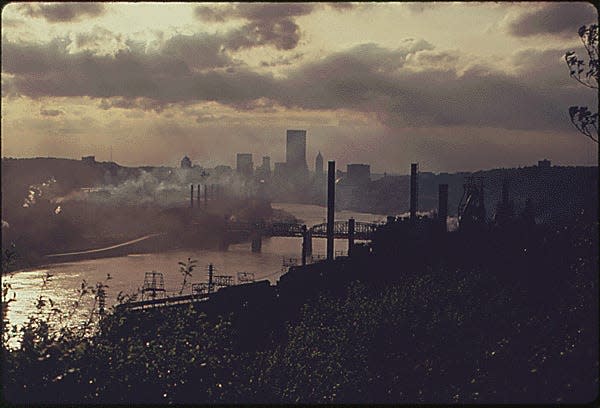 SMOKE FROM INDUSTRY CREATES A HAZE WHICH LINGERS OVER THE CITY OF PITTSBURGH, PENNSYLVANIA, ON THE HORIZON. IN THE FOREGROUND ON BOTH SIDES OF THE MONONGAHELA RIVER, ARE PLANTS OWNED BY THE JONES AND LAUGHLIN STEEL CORPORATION. THE POLLUTION HAS CONTINUED SINCE THIS PICTURE WAS TAKEN. CLEANUP EFFORTS HAVE BEEN SCHEDULED AT THE JONES AND LAUGHLIN PLANTS