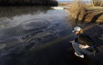 In this Wednesday, Feb. 5, 2014 photo, Amy Adams, North Carolina campaign coordinator with Appalachian Voices dips her hand into the Dan River in Danville, Va. as signs of coal ash appear in the river. Duke Energy estimates that up to 82,000 tons of ash has been released from a break in a 48-inch storm water pipe at the Dan River Power Plant in Eden N.C. Over the last year, environmental groups have tried three times to use the federal Clean Water Act to force Duke Energy to clear out leaky coal ash dumps. Each time, the N.C. Department of Environment and Natural Resources has effectively halted the lawsuit by intervening at the last minute to assert its own authority to take enforcement action. In two cases, the state has proposed modest fines but no requirement that the nation’s largest electricity provider actually clean up the coal ash ponds. The third case is pending. (AP Photo/Gerry Broome)