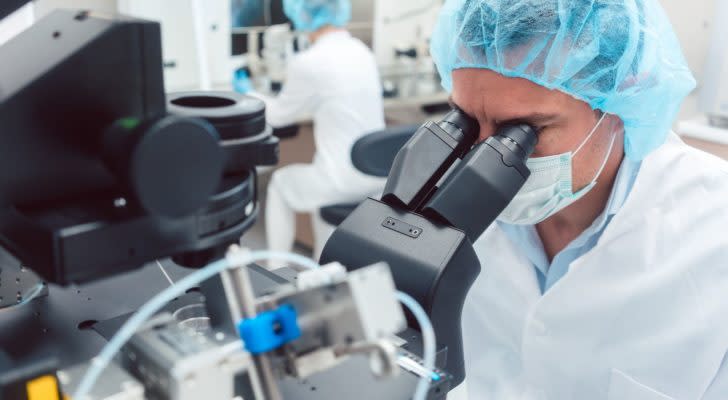 A scientist in medical gear peers through a microscope.