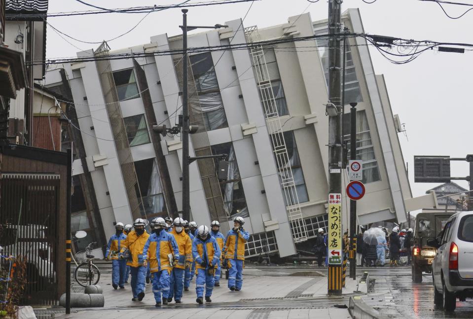 Firefighters walk near a fallen building following earthquakes in Wajima, Ishikawa prefecture, Japan Wednesday, Jan. 3, 2024. (Kyodo News via AP)