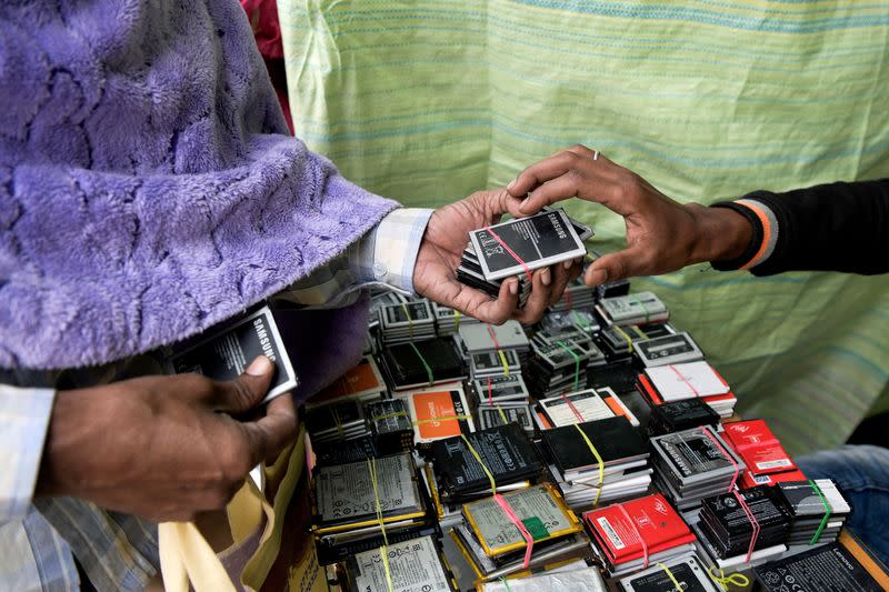 Man buys an old battery from a seller at a stall in a makeshift market in South Bishnupur