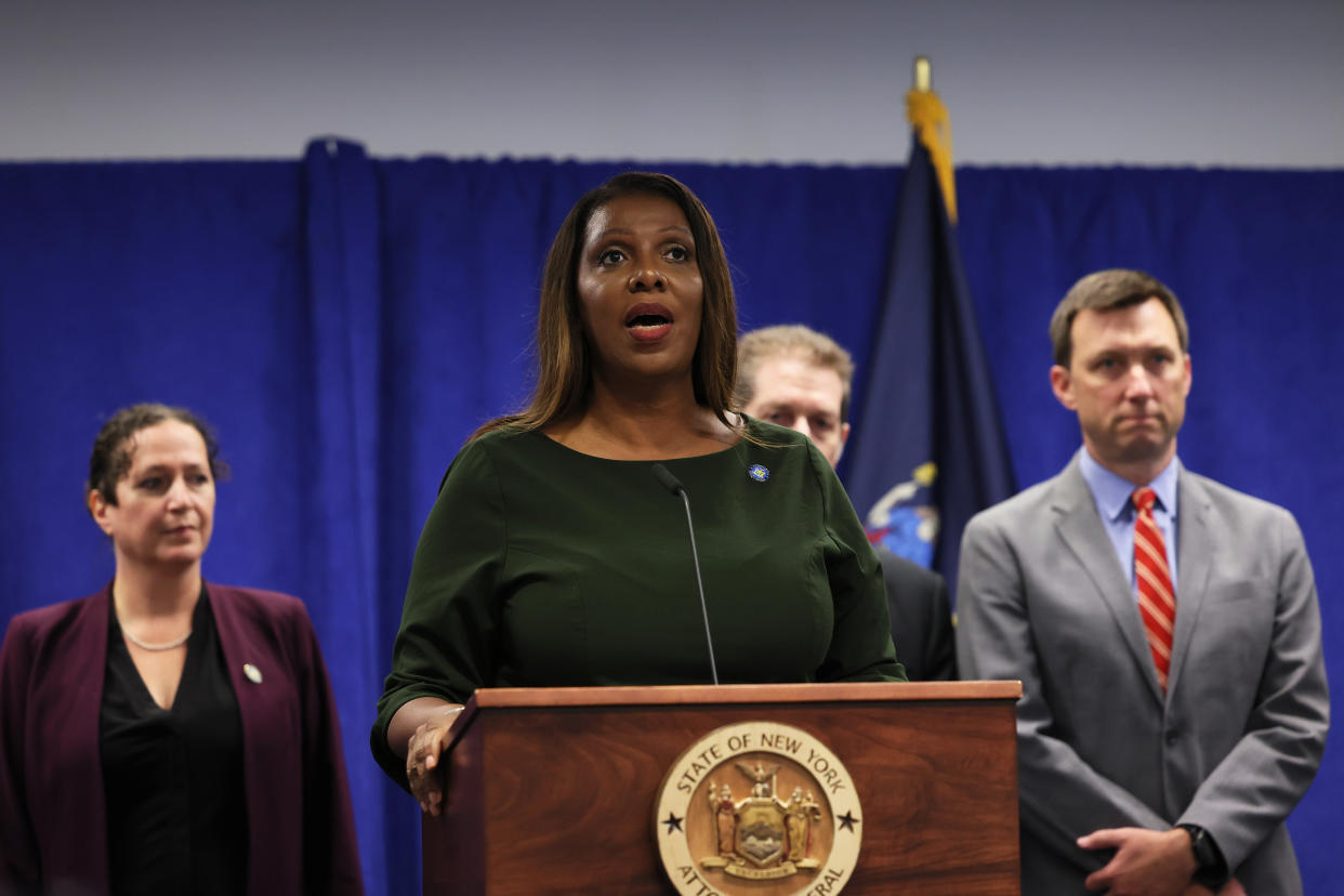 Attorney General Letitia James, flanked by a woman and two men, at the microphone at a dais reading: State of New York, Attorney General. 