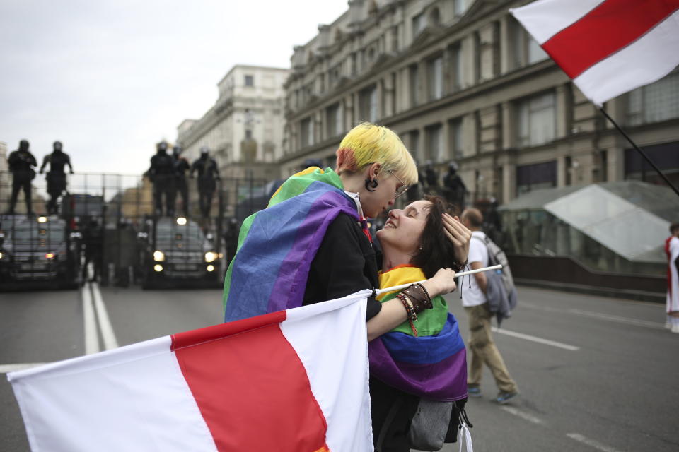 LGBT activists react together, with an old Belarusian national flag, in front of a police barricade blocking a street during an opposition rally to protest the official presidential election results in Minsk, Belarus, Sunday, Sept. 6, 2020. Sunday's demonstration marked the beginning of the fifth week of daily protests calling for Belarusian President Alexander Lukashenko's resignation in the wake of allegedly manipulated elections. (AP Photo/TUT.by)