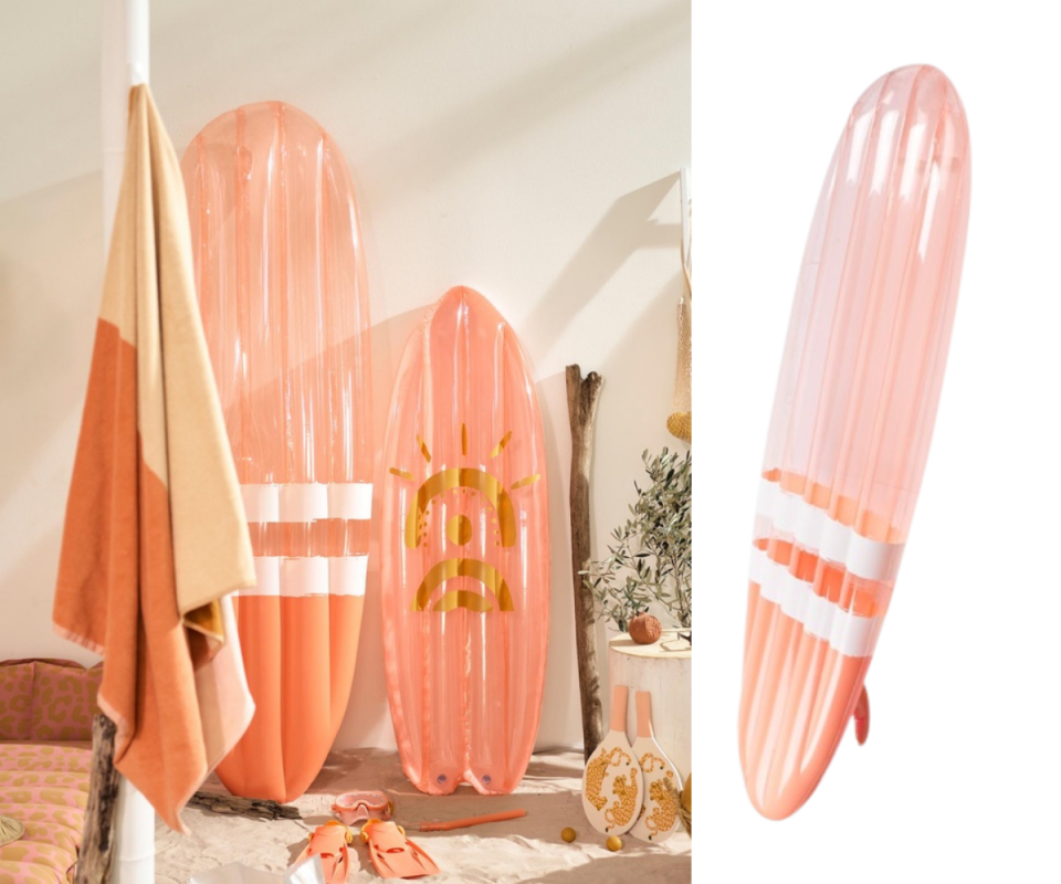 A peach-coloured inflatable surfboard standing upright against a beige background with a peach and orange umbrella.