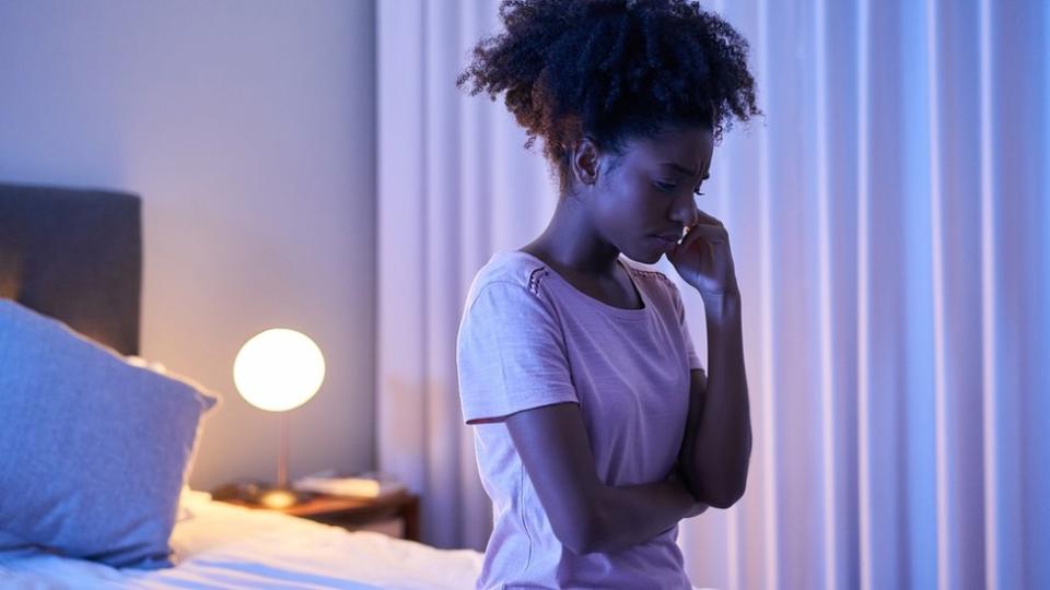 A young woman sitting alone in her bedroom at night.