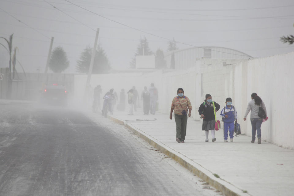 FILE - People walk on the ash-covered streets of San Andres Cholla, Mexico April 18, 2016, after the Popocatepetl volcano erupted overnight, spewing ash on nearby towns. The sacred understanding of “El Popo” varies from town to town, but many agree that the volcano does not threaten their lives. (AP Photo/Pablo Spencer, File)