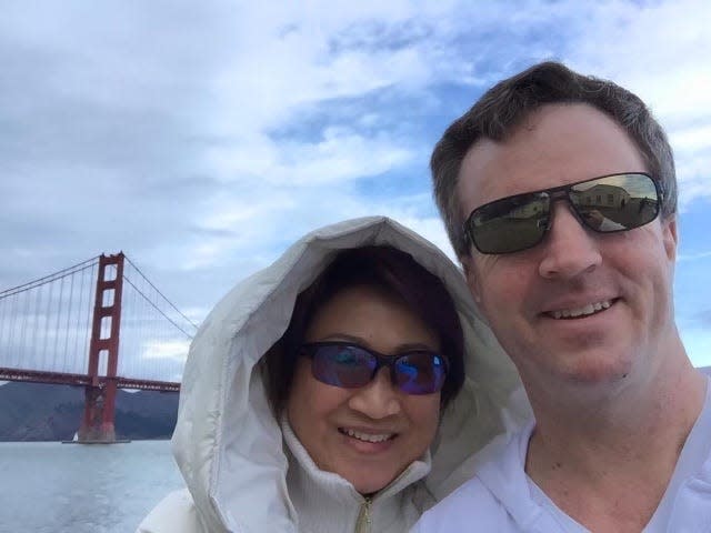 A couple wearing sunglasses takes a selfie in front of the Golden Gate Bridge