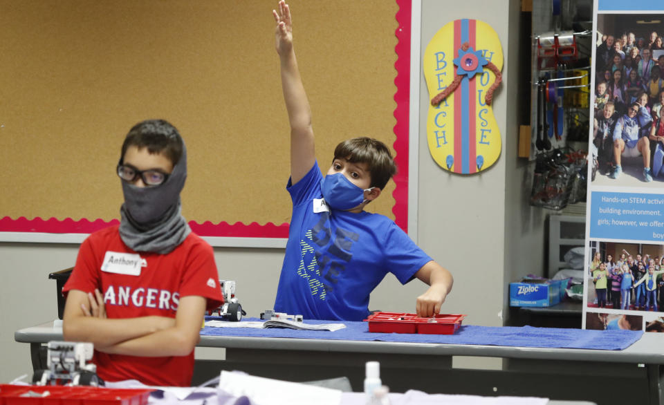 FILE - In this July 14, 2020, file photo, amid concerns of the spread of COVID-19, Aiden Trabucco, right, wears a mask as he raises his hand to answer a question behind Anthony Gonzales during a summer STEM camp at Wylie High School in Wylie, Texas. School districts that plan to reopen classrooms in the fall are wrestling with whether to require teachers and students to wear face masks — an issue that has divided urban and rural schools and yielded widely varying guidance. (AP Photo/LM Otero, File)
