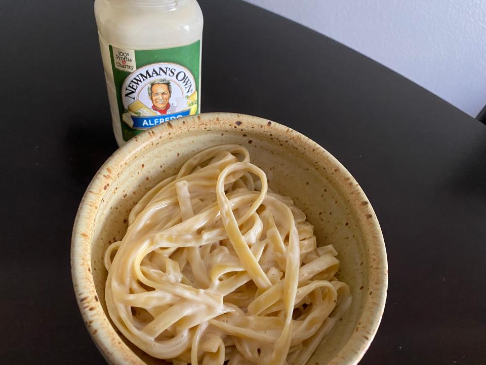 A bowl of pasta with Newman's Own Alfredo sauce jar in background