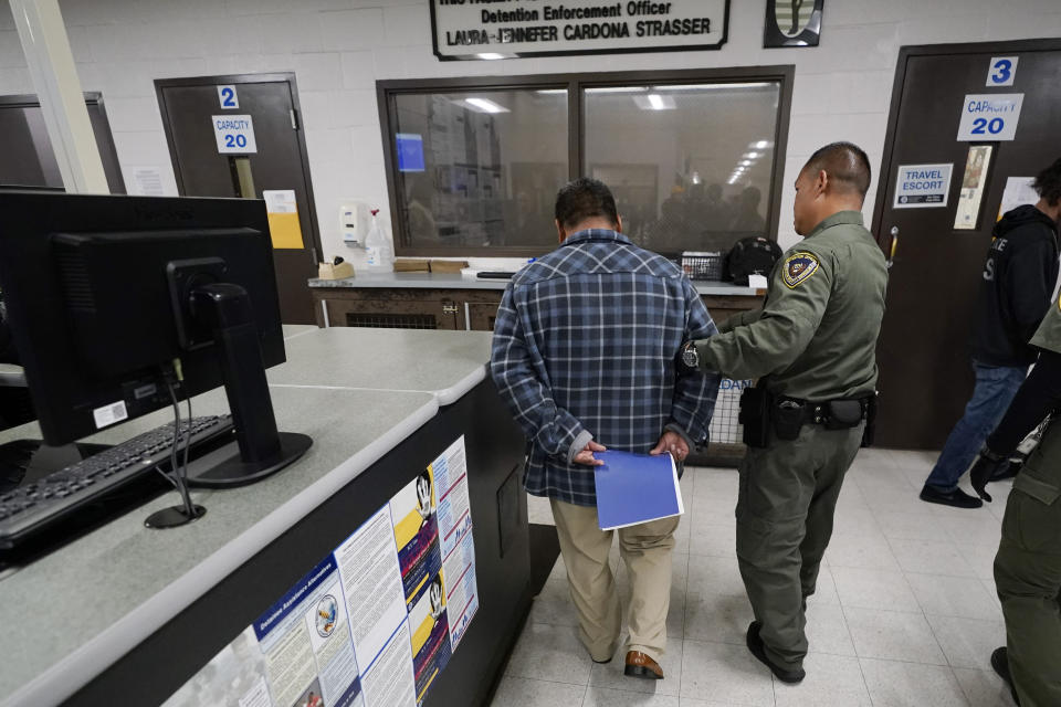 An officer escorts a man detained in an immigration and customs processing facility, Wednesday, March 15, 2023, in San Diego. Some asylum-seekers who crossed the border from Mexico are waiting 10 years just for a court date. The Border Patrol released people with notices to appear at a U.S. Immigration and Customs Enforcement office. The move saved the Border Patrol untold hours processing court papers, but it left the job to an agency that had no extra staff for the increased workload. (AP Photo/Gregory Bull)